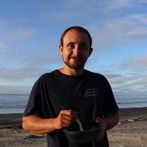 photo of Jay at a beach with some camping food - he is smiling