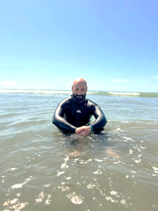 photograph of Jonathan Stone in water at a beach - he is in a wet suit and smiling