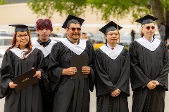 5 students posing for a photo in their graduation regalia outdoors.