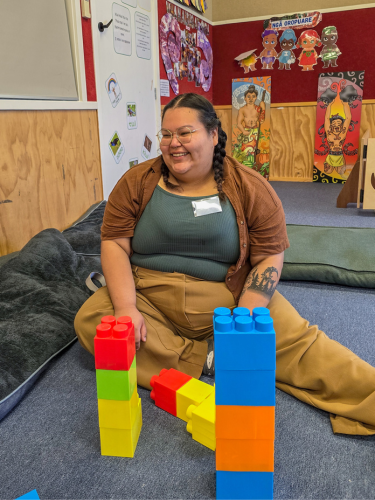 Student Emma Robinson sitting on the floor playing with Maori children at one of the Language Nests