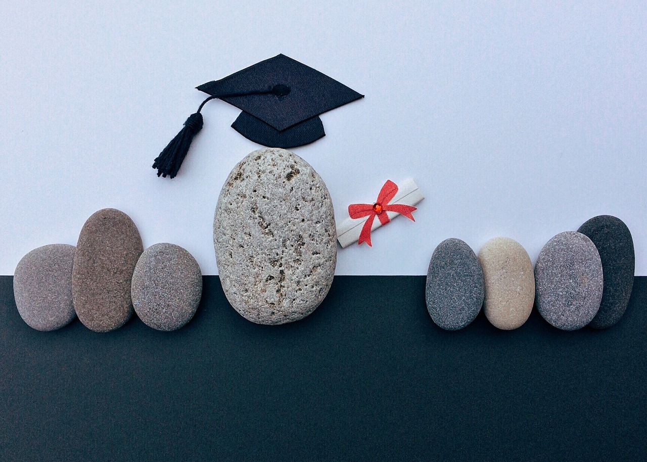 illustrative image of stones as people, the central one is wearing a graduation cap and carrying a diploma